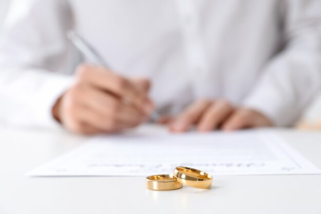 Man,Signing,Marriage,Contract,And,Wedding,Rings,On,Desk,,Selective